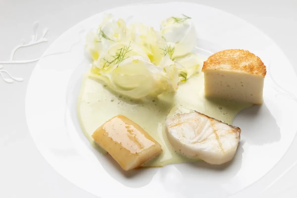 Un plat composé de légumes, de poisson et d'une sauce verte sur une assiette blanche