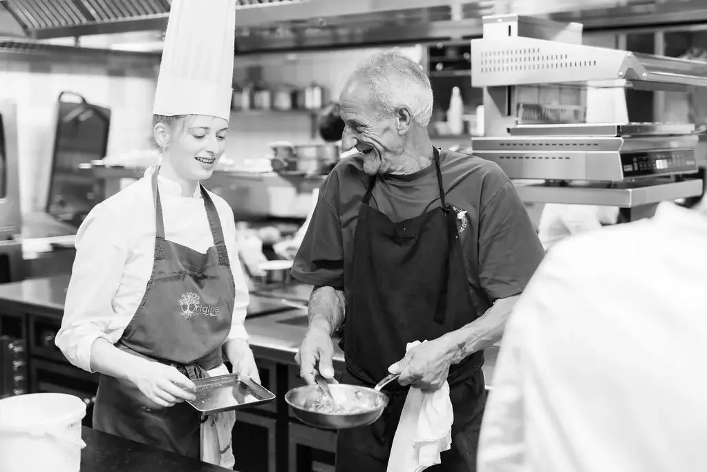Deux personnes en tenue de cuisine échangent en souriant dans une cuisine professionnelle