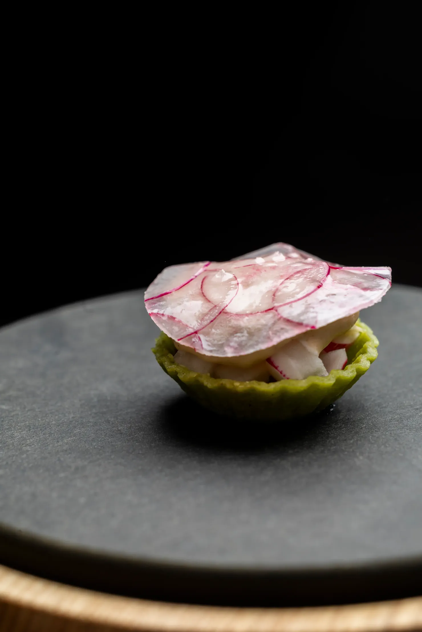 Petite tarte verte garnie de radis tranchés, posée sur une assiette noire