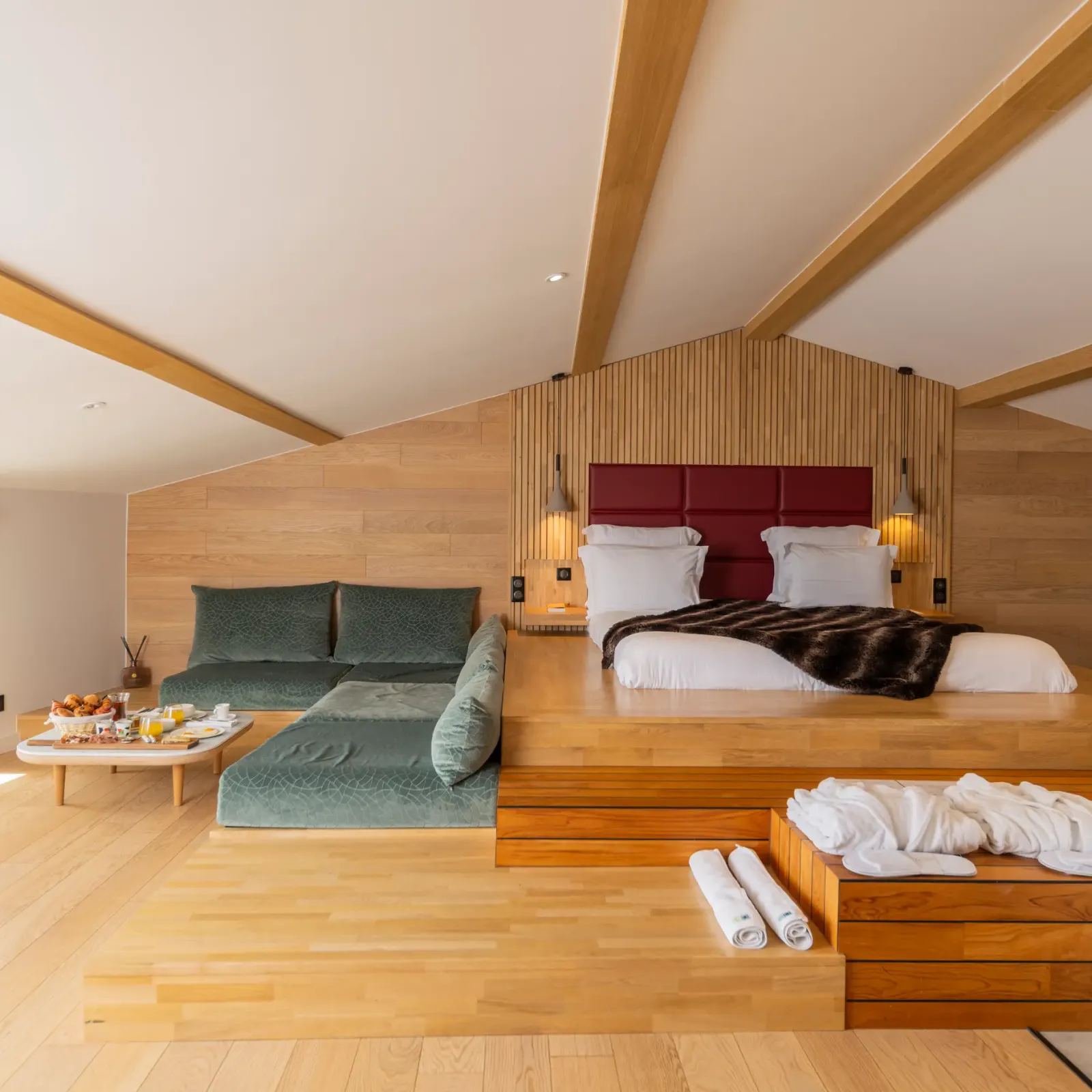 Spacious room with elevated main bed, sofa, coffee table with food and drinks, and windows offering an outdoor view.