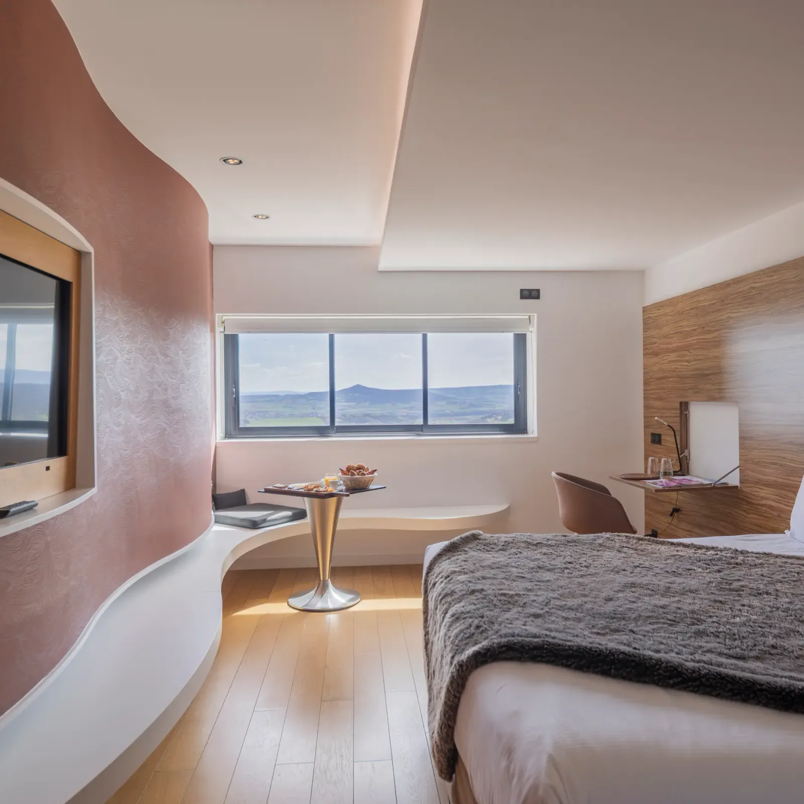 Chambre moderne avec lit, télévision, table avec fruits et vue panoramique sur le paysage extérieur