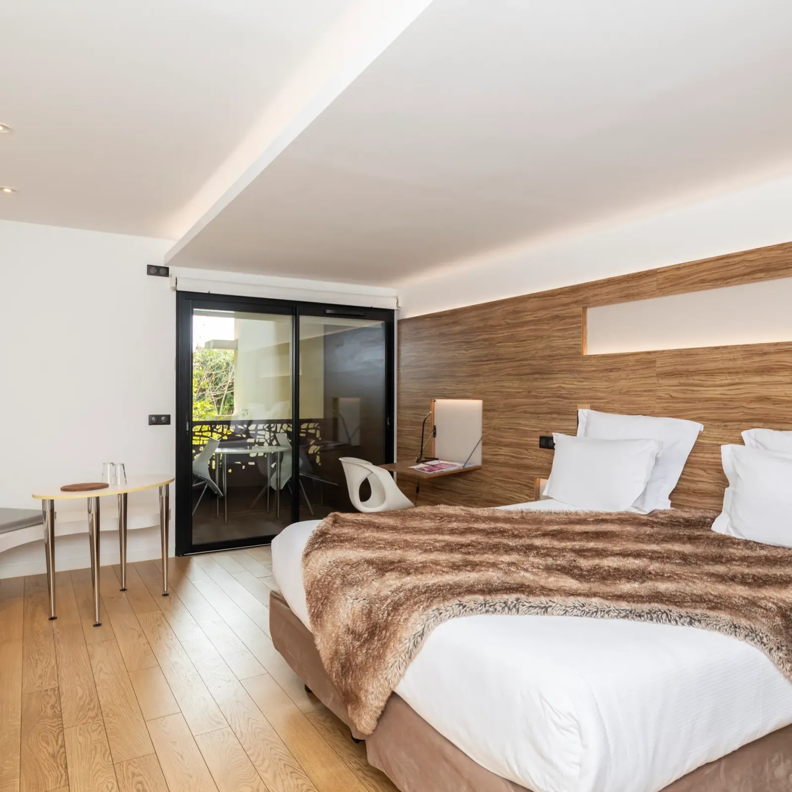 Chambre moderne avec un lit double, une table de chevet, une porte-fenêtre donnant sur un balcon et un mur en bois