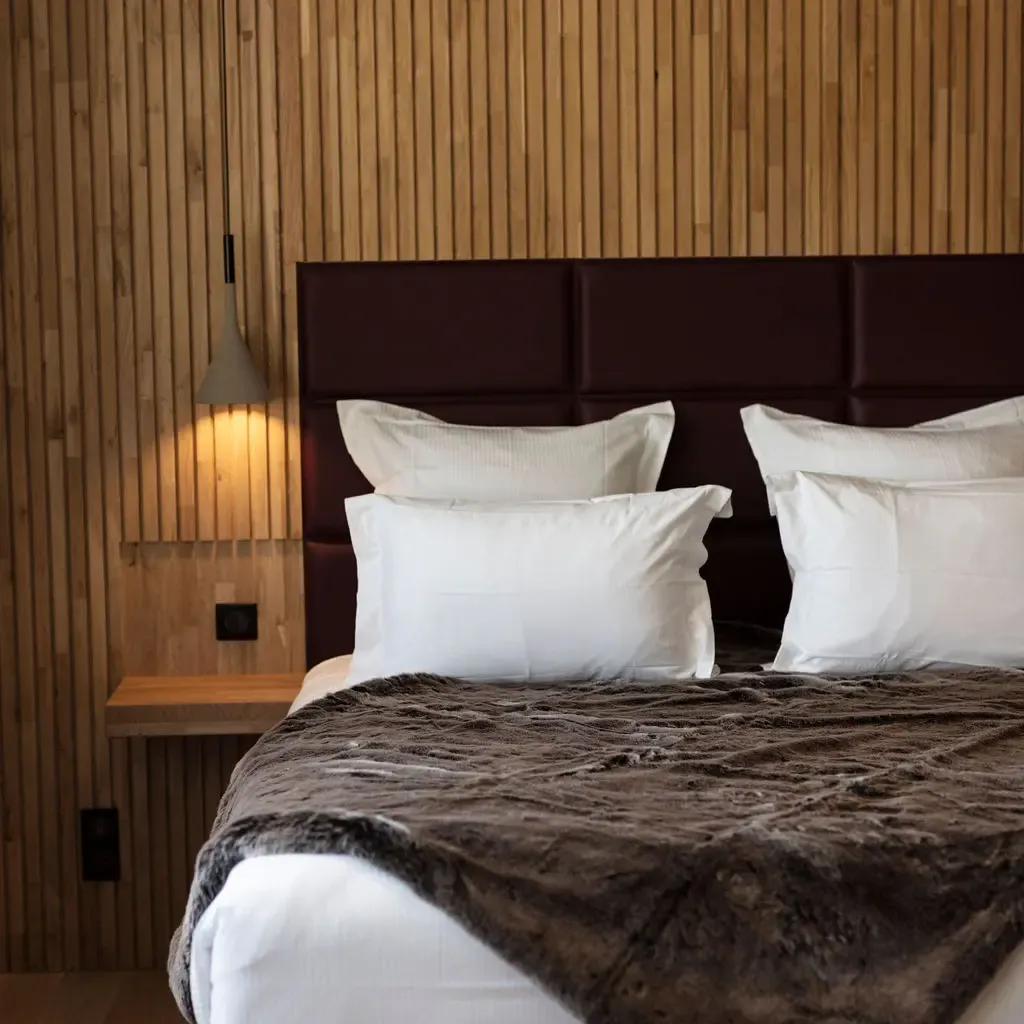 Bed with a brown leather headboard, white sheets, and a gray blanket in a room with wooden walls