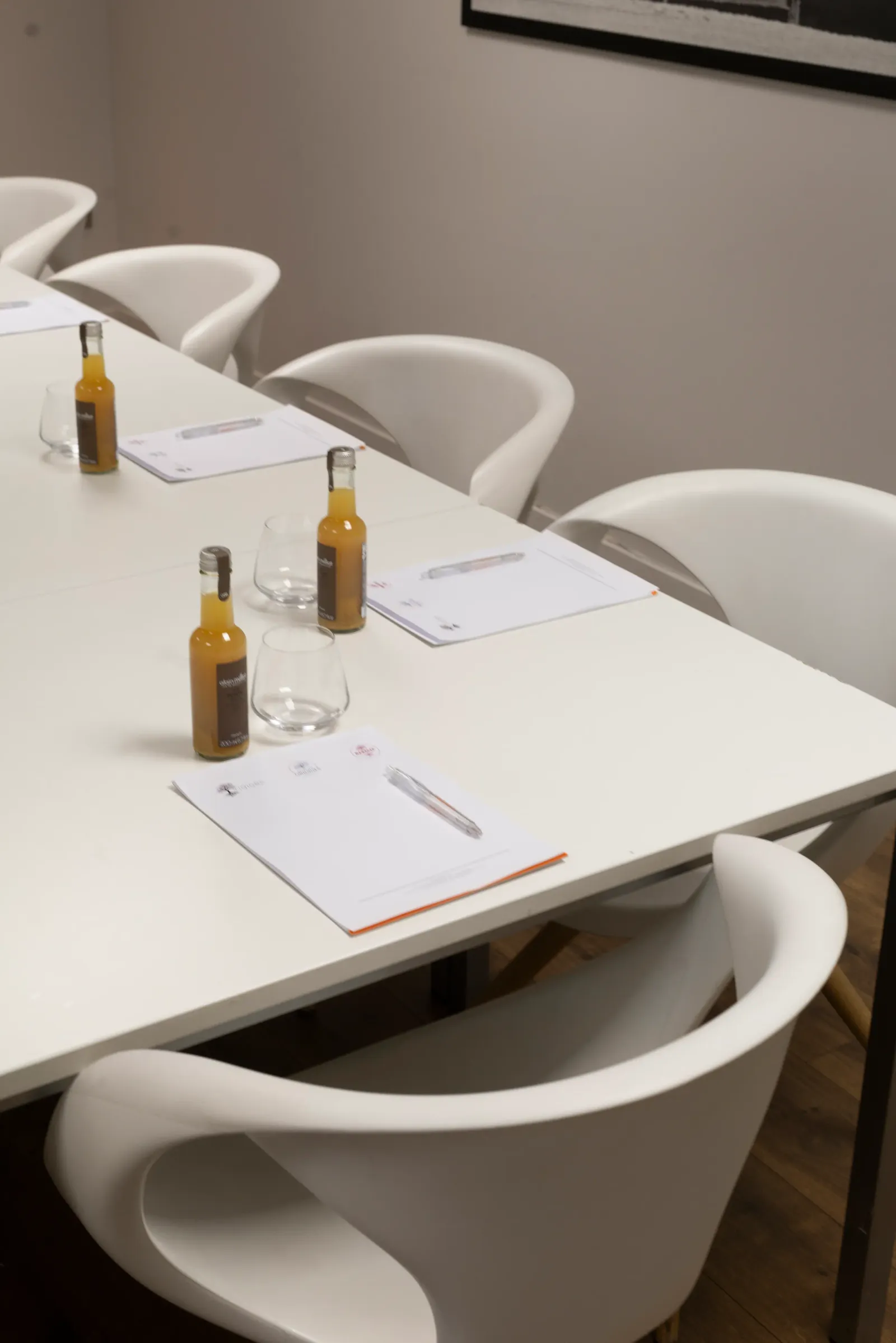 Table blanche avec des bouteilles de boisson, des verres et des documents, entourée de chaises blanches