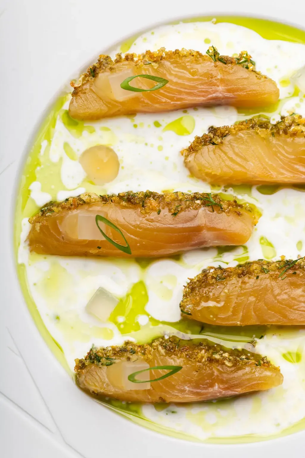 Quatre filets de poisson garnis d'herbes et de panko, disposés sur une sauce verte et blanche dans une assiette blanche