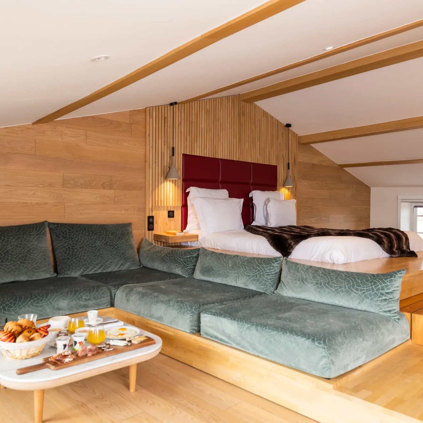 Room with double bed and green sofa, coffee table with breakfast tray, wooden walls and sloping ceiling