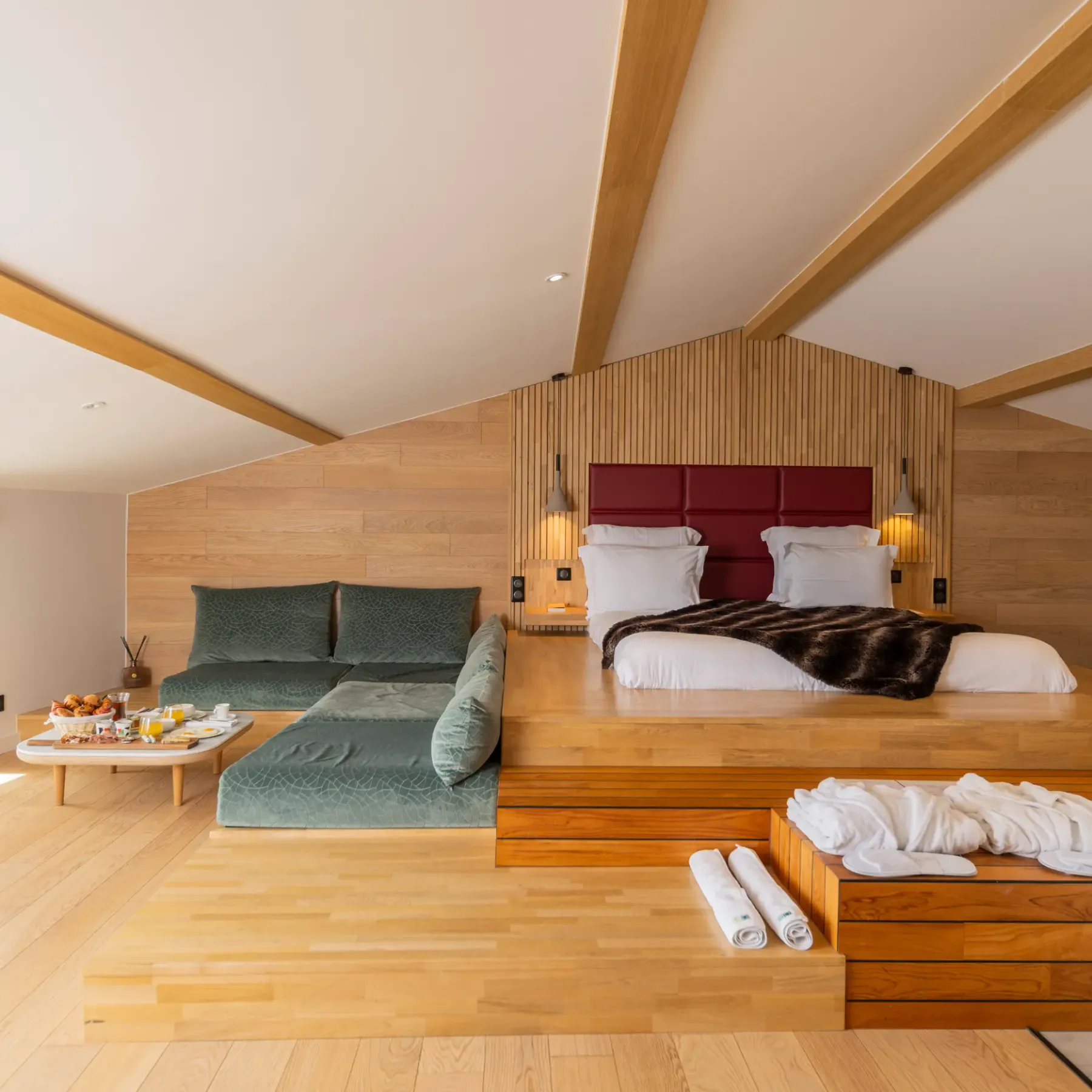 Spacious room with elevated main bed, sofa, coffee table with food and drinks, and windows offering an outdoor view.