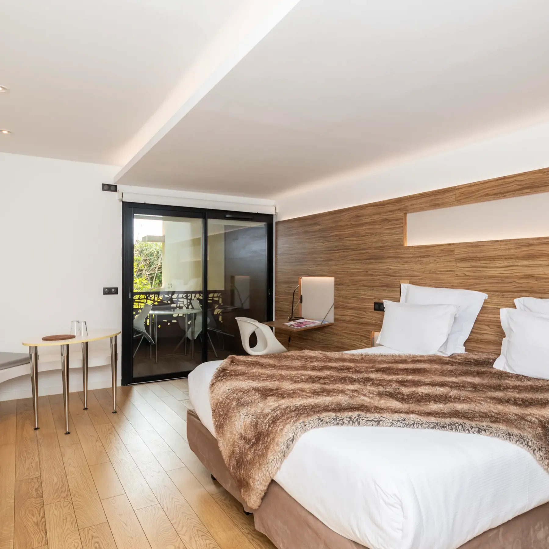 Modern room with a double bed, a bedside table, a French door leading to a balcony, and a wooden wall.