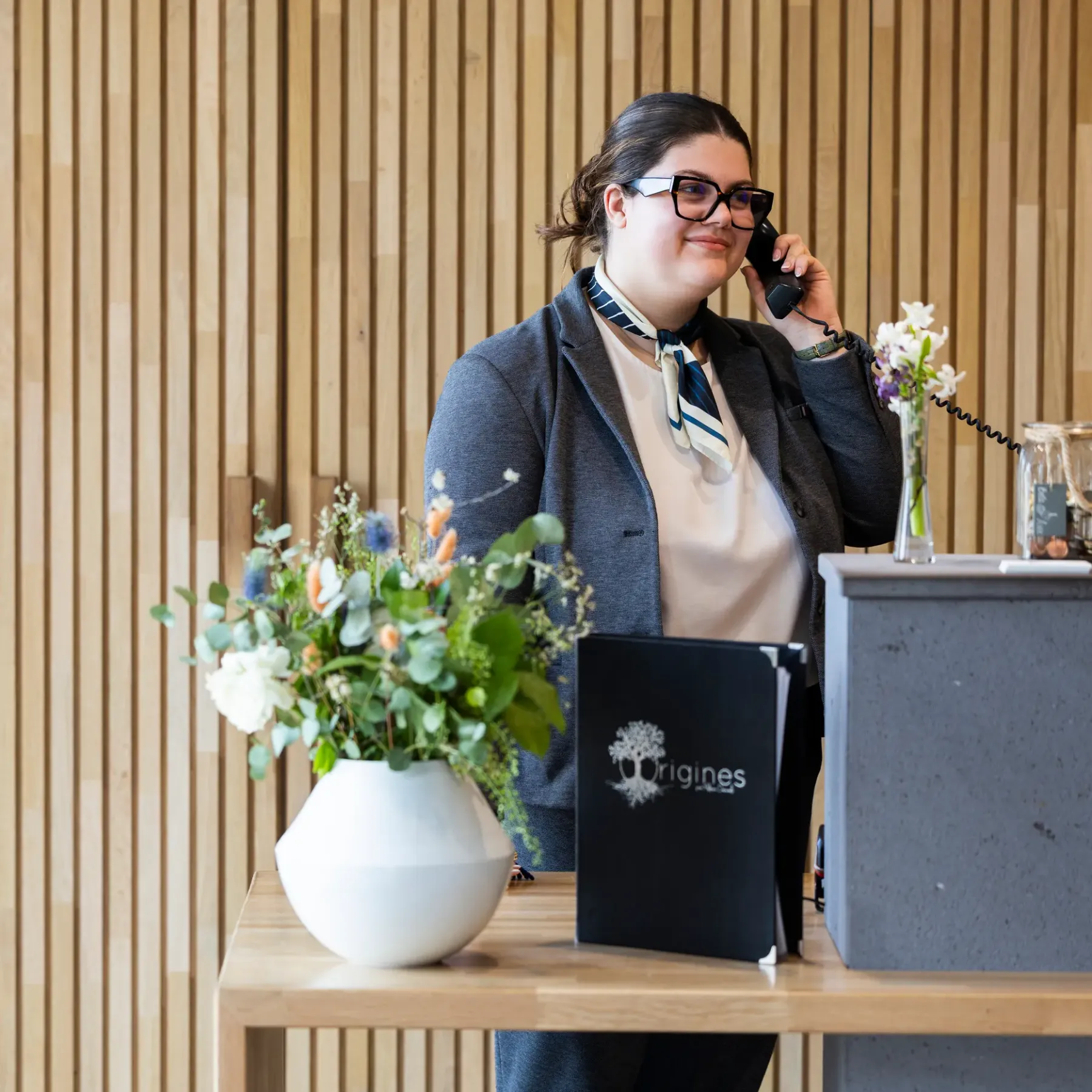 A person on the phone behind a counter with a vase of flowers and a black book