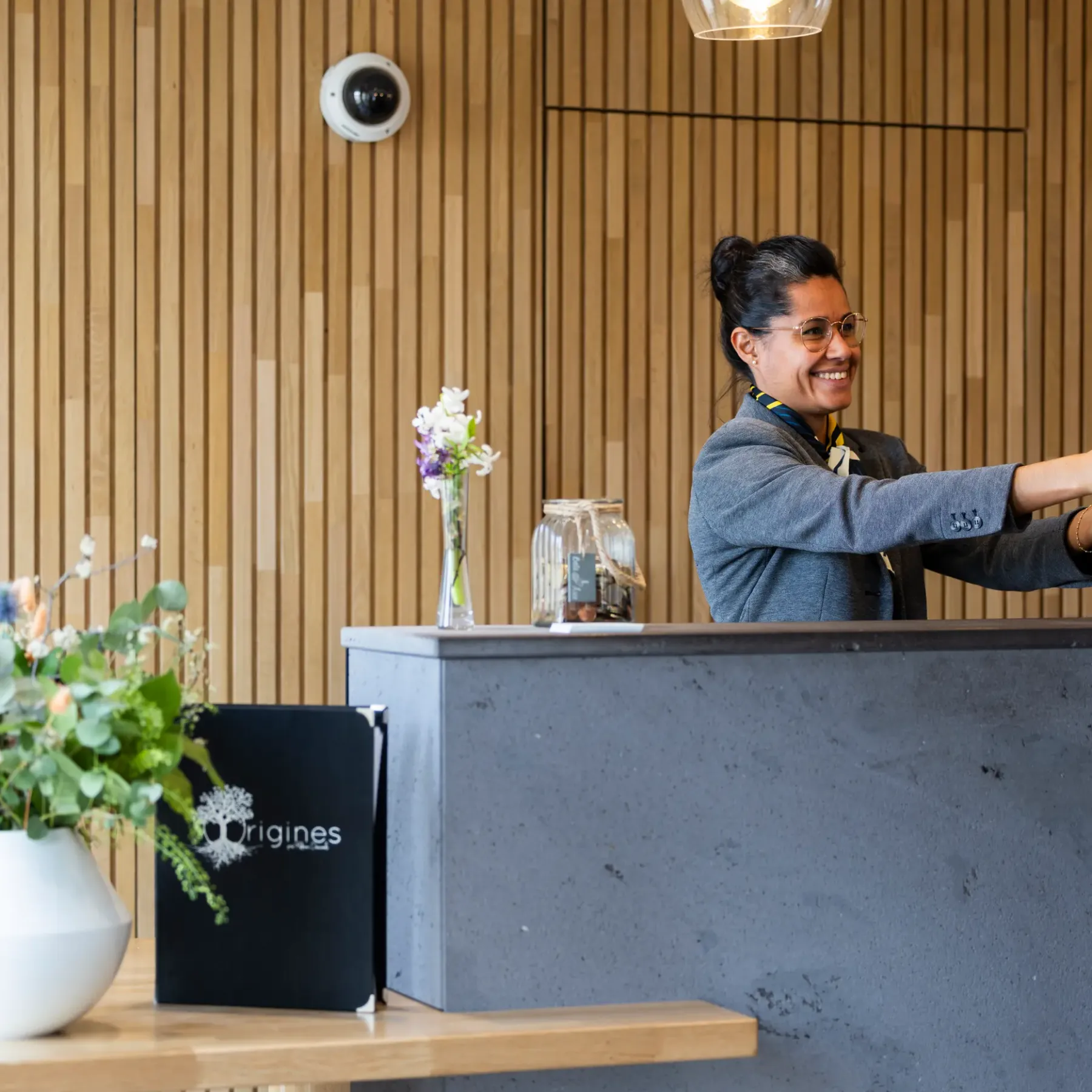 A person behind a counter hands a card to a customer in an indoor space with wooden walls and flowers.