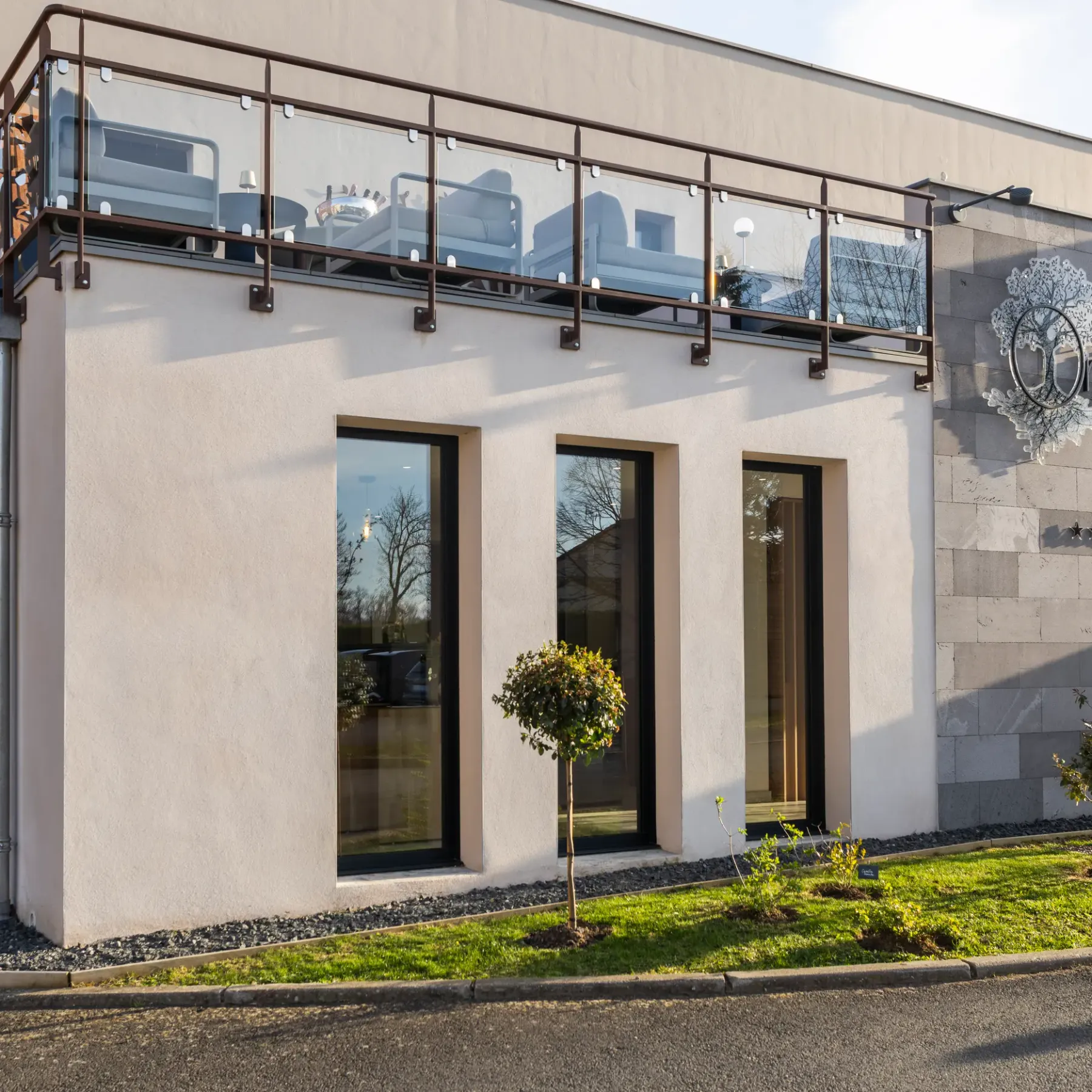 Modern building with a stone and stucco facade, a glass door, and a balcony with a metal railing, displaying the name "Origines"