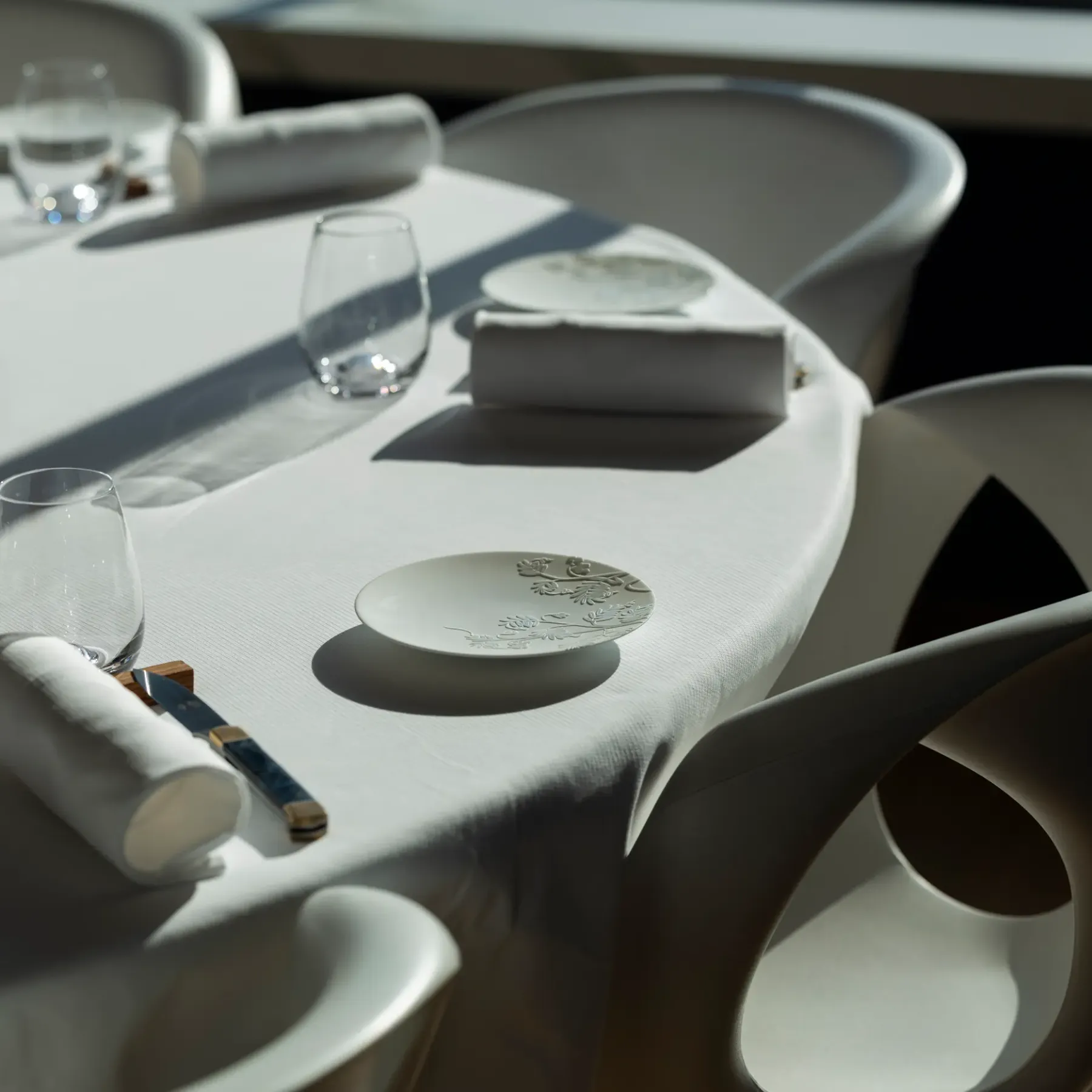 Table set with glasses, cutlery, and folded napkins on a white tablecloth.