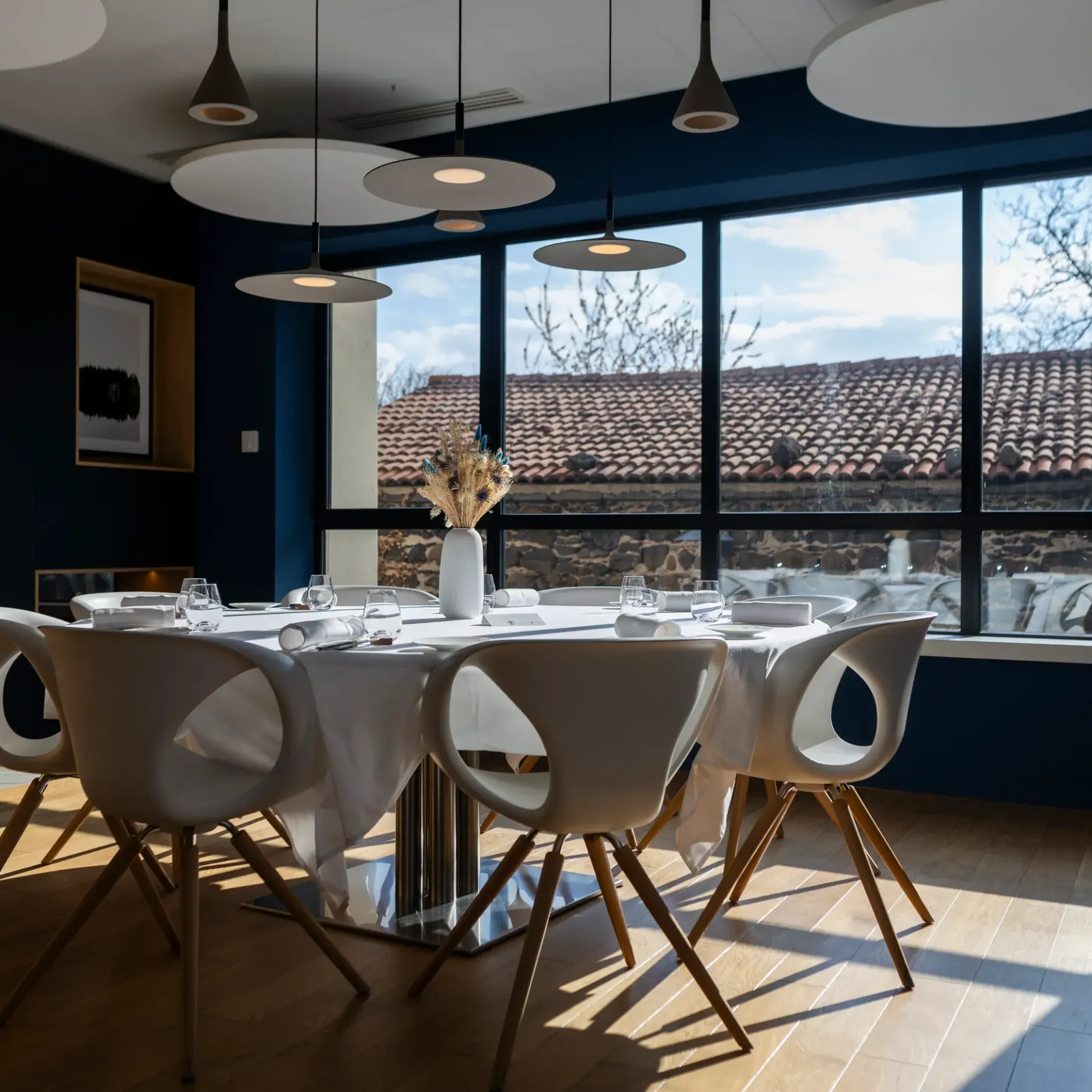 A round table with modern chairs in front of a large window overlooking a tiled roof