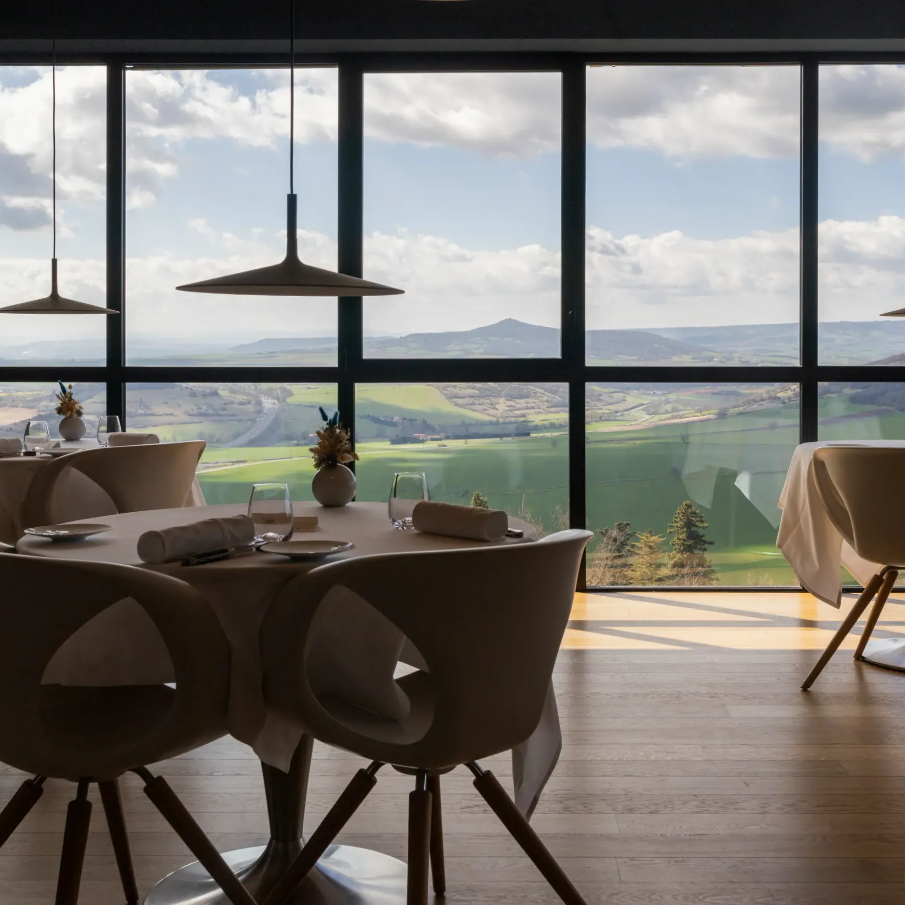 A dining room with a large bay window offering a view of a rolling landscape and distant mountains.