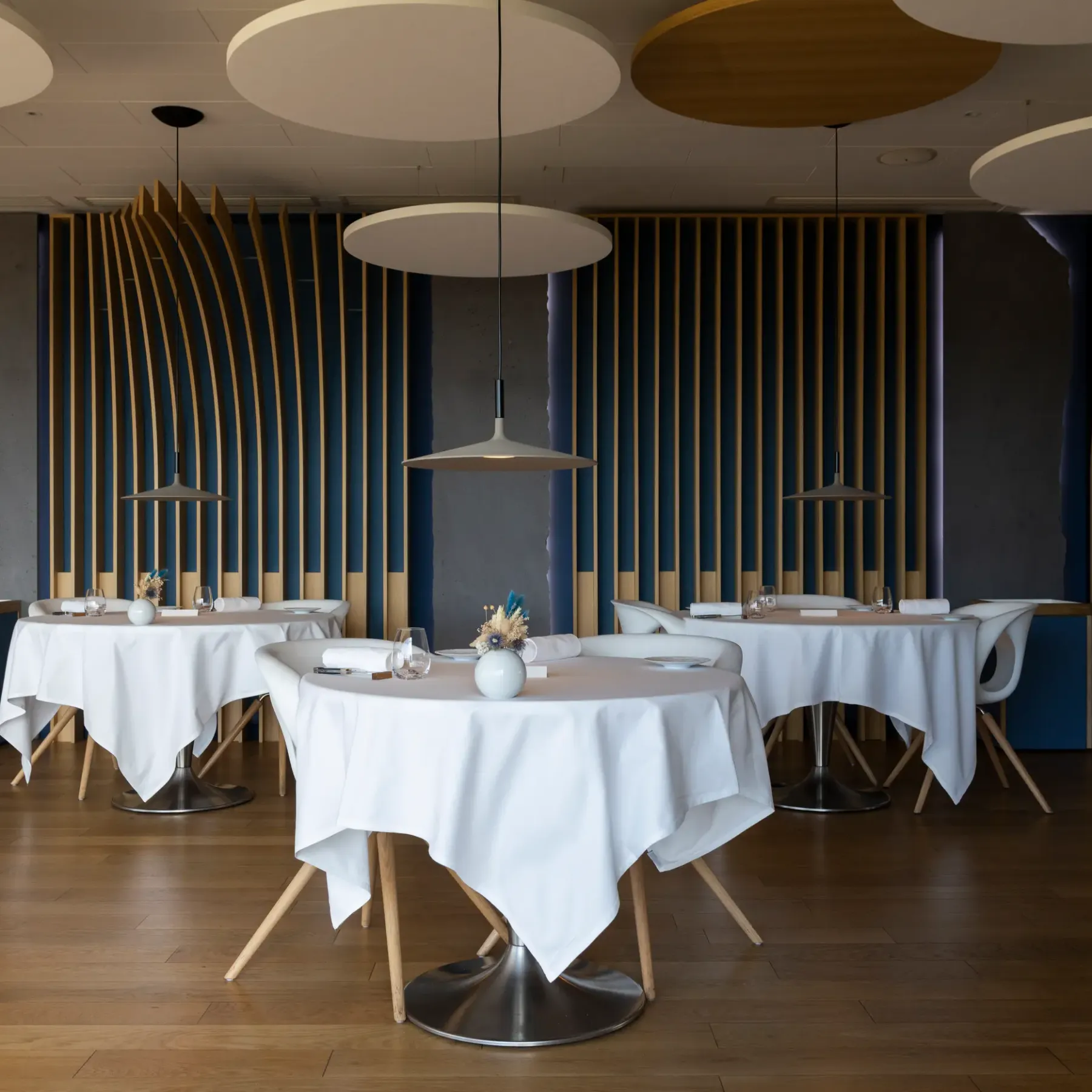 Restaurant room with round tables covered in white tablecloths, modern chairs, and hanging light fixtures.