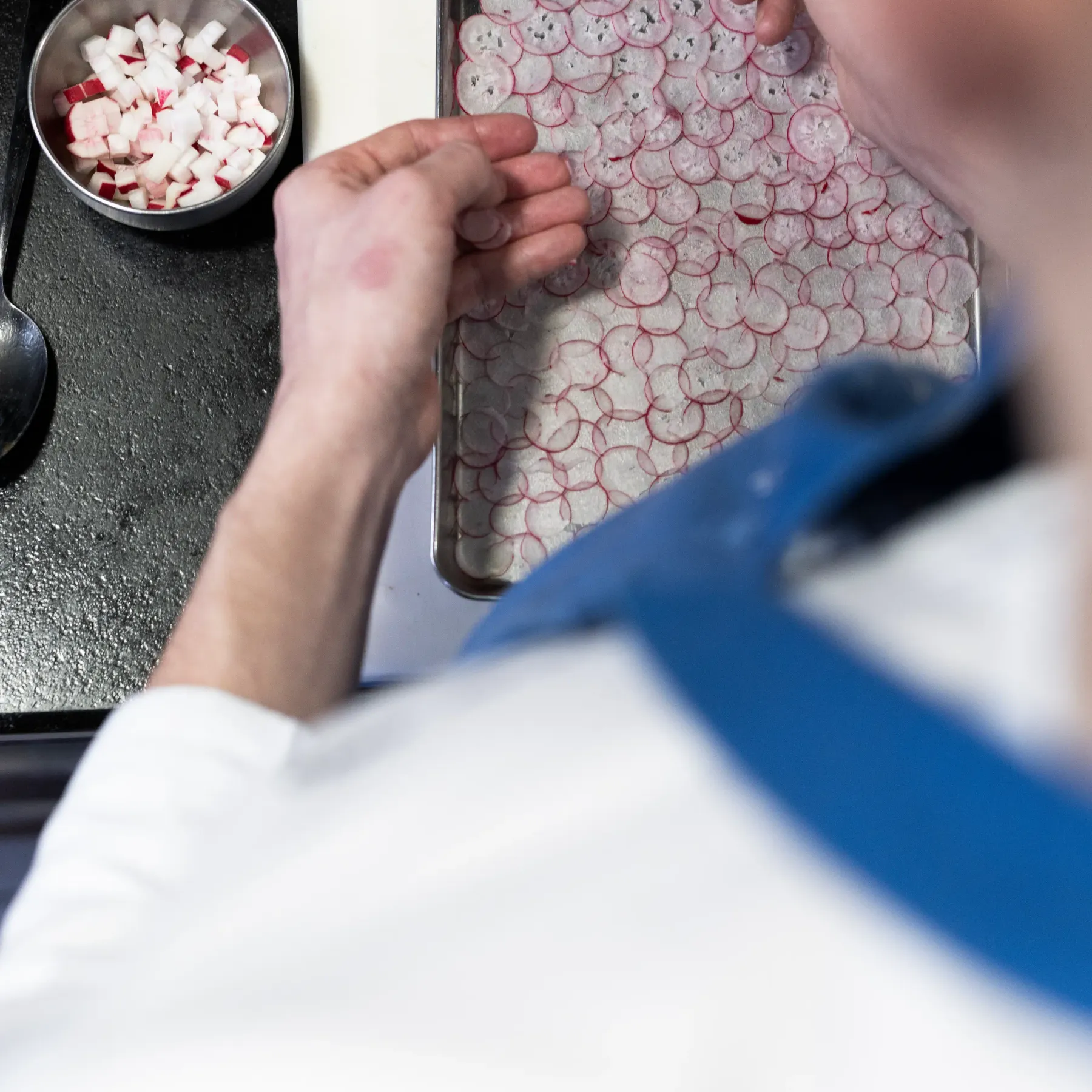 A person cuts radish slices and arranges them on a baking tray.