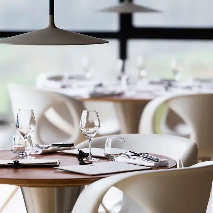 Table set with glasses, cutlery, and napkins, under hanging lamps in a restaurant with large glass windows.