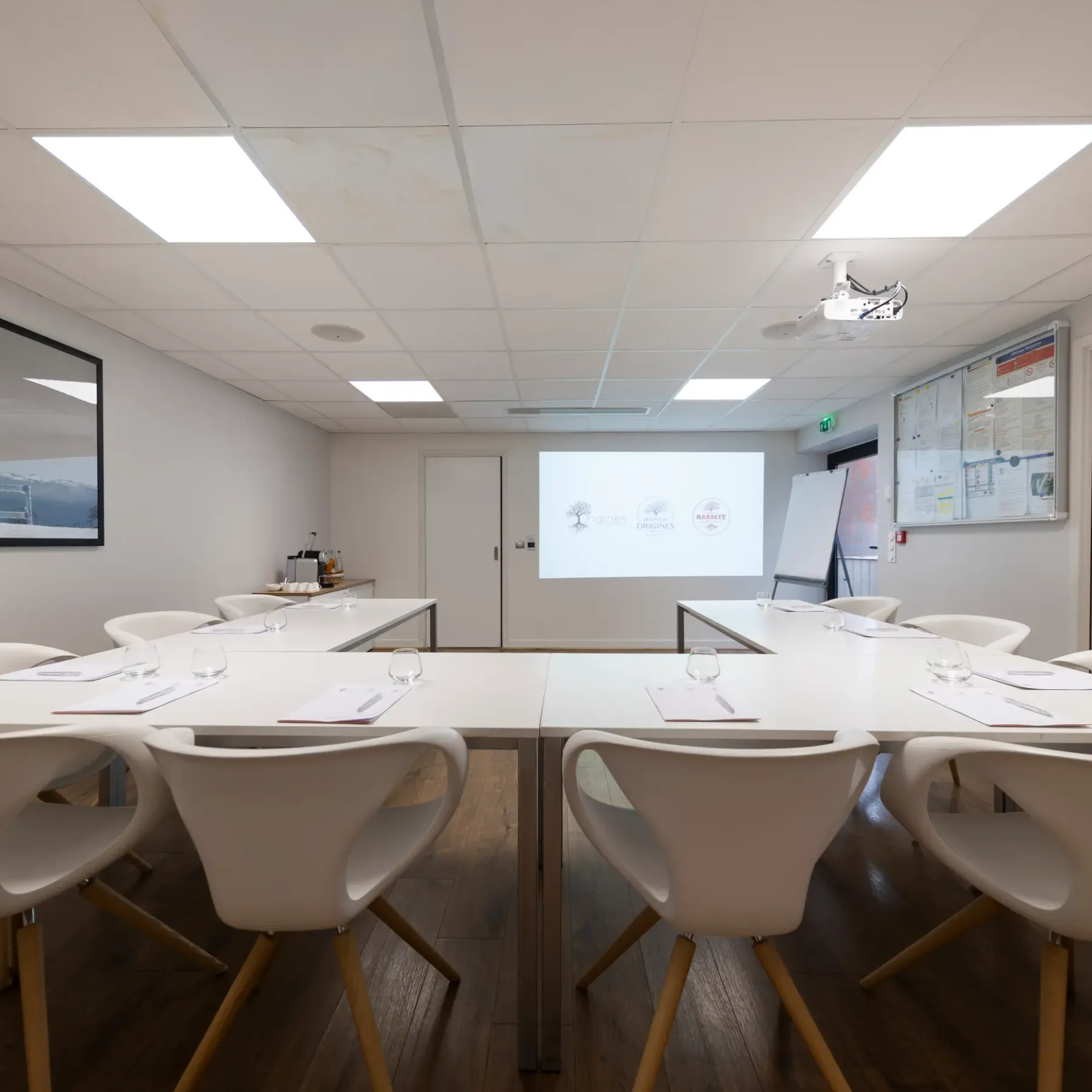 Meeting room with oval table, white chairs, and projector displaying logos on a screen