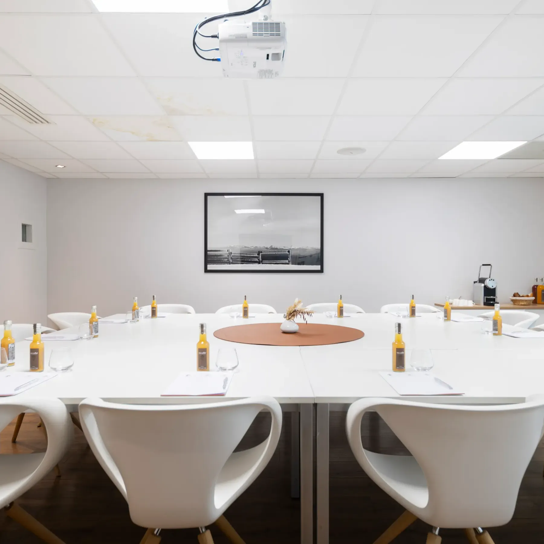 Meeting room with a round table, white chairs, water bottles, and a ceiling-mounted projector