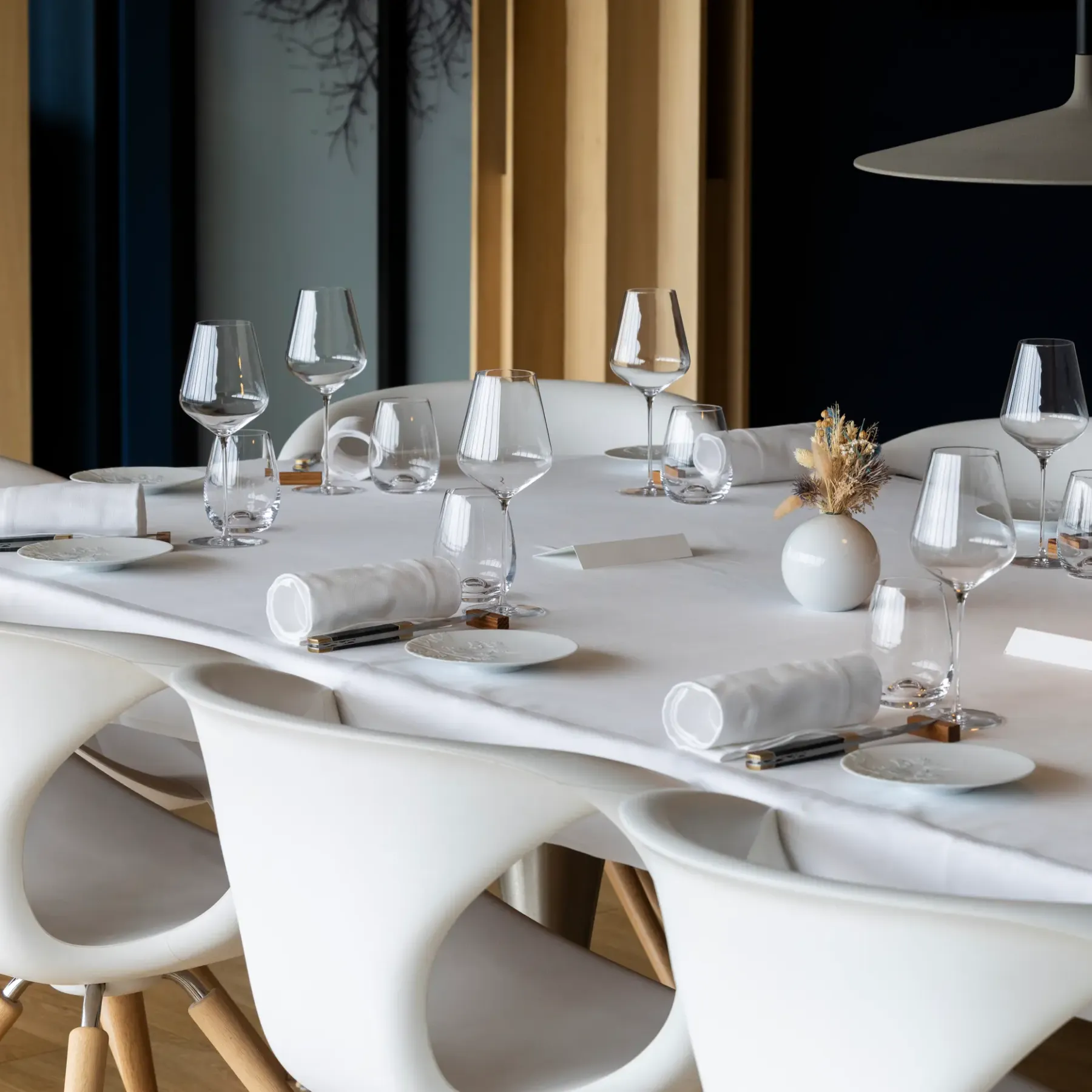 White round table with wine glasses, napkins, and cutlery, surrounded by modern chairs in an elegant interior