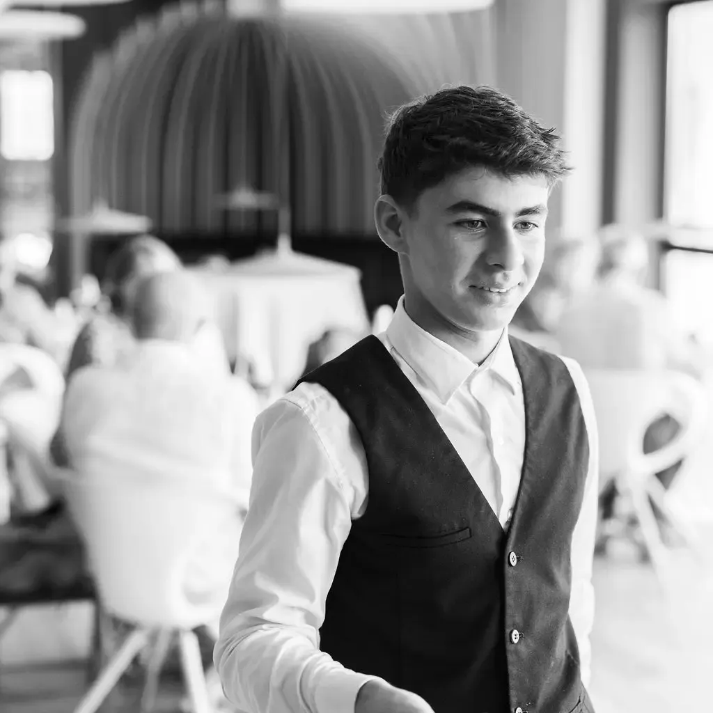 Young man in black jacket and white shirt serving customers in a restaurant