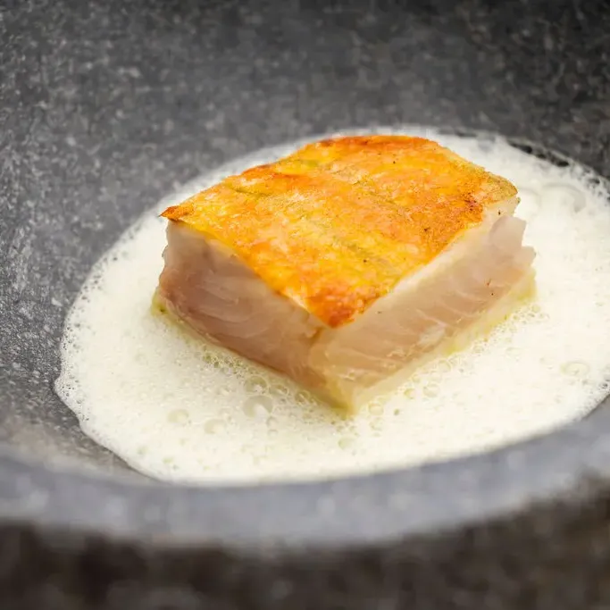 A piece of poached fish in a white liquid, presented in a cast-iron pan