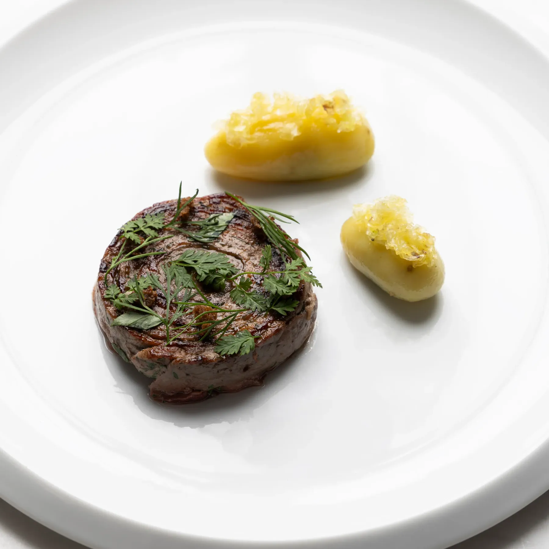 A grilled steak topped with parsley and two fried potatoes on a white plate