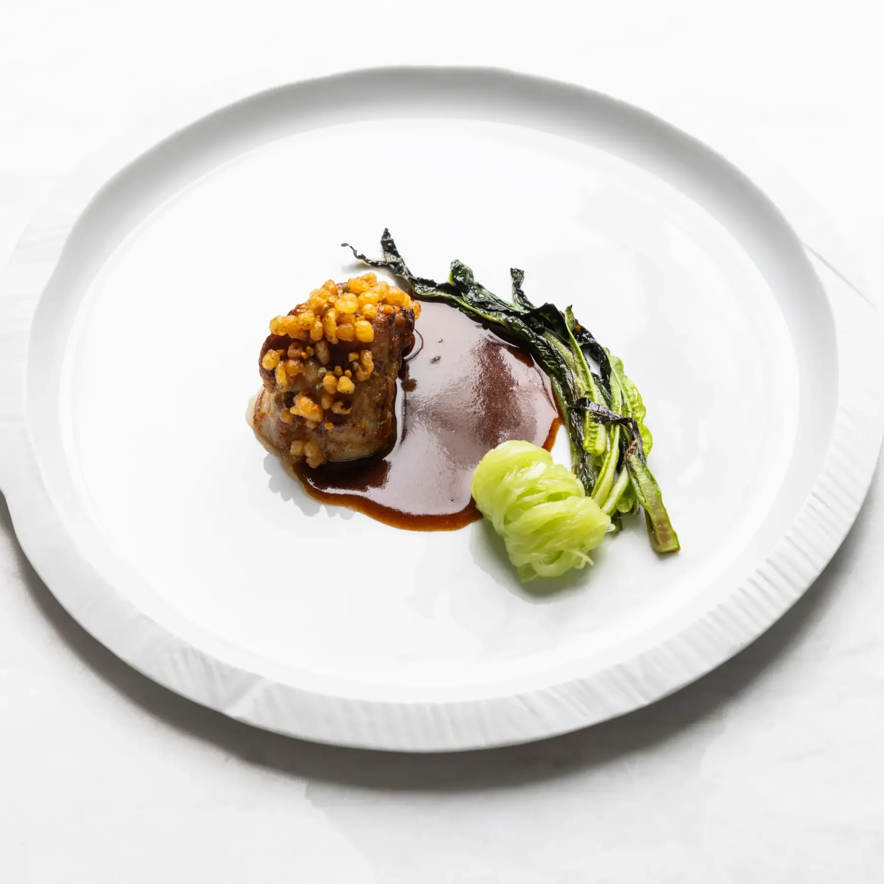 A dish consisting of a piece of meat covered with seeds, served with green vegetables and a sauce, presented on a white plate.