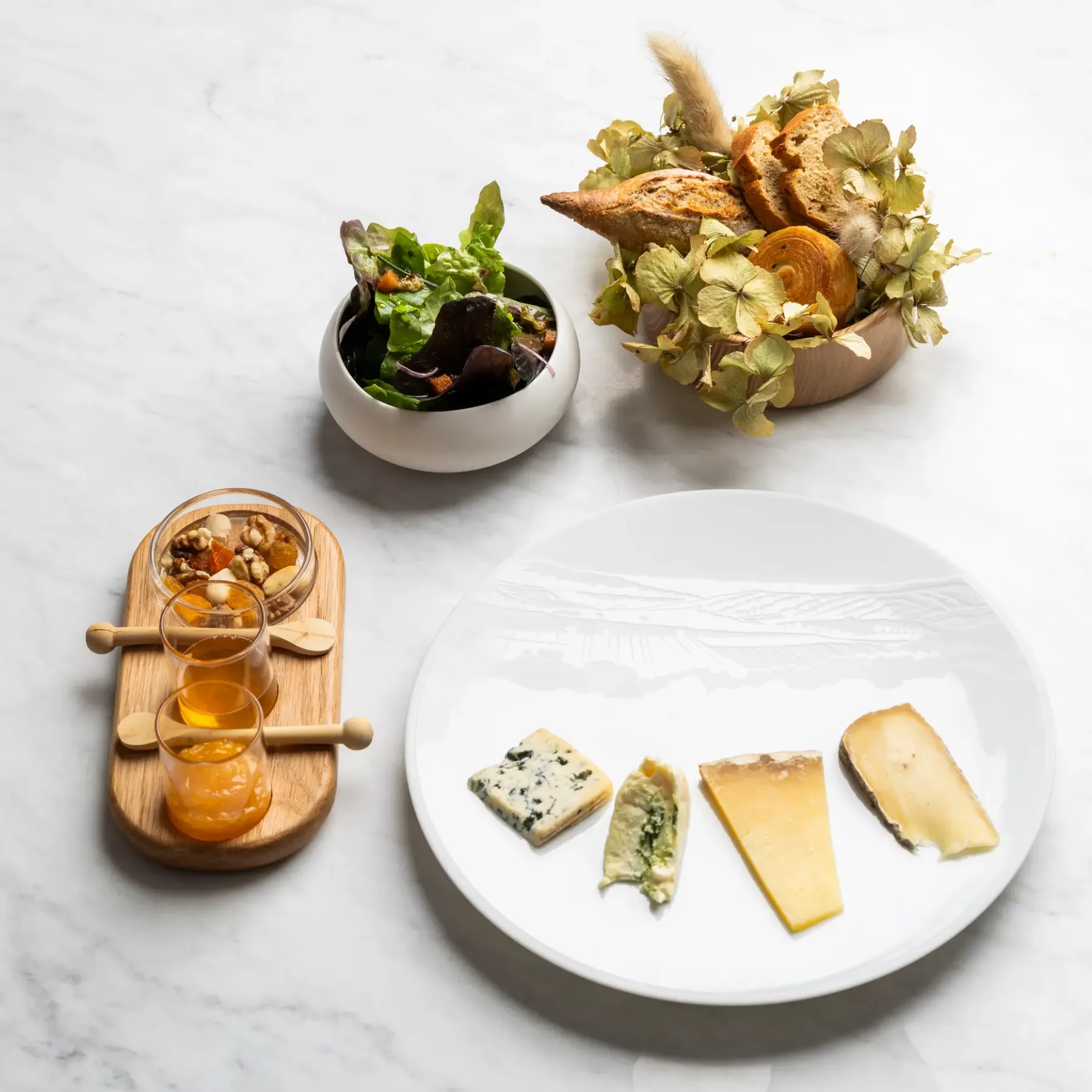 Cheese platter with accompaniments, salad, and bread on a marble table