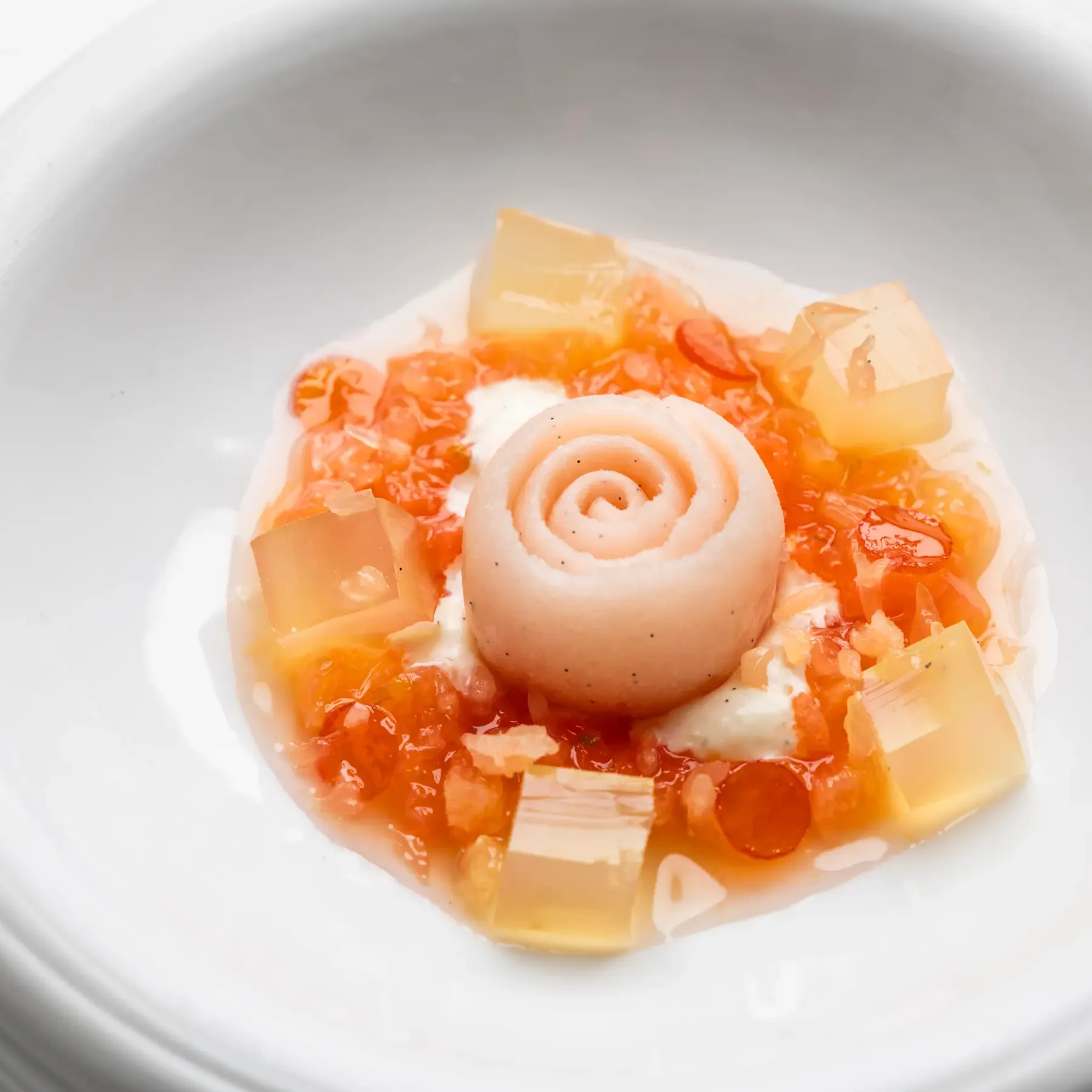 A white bowl contains a culinary preparation with pieces of vegetables and a rolled ball of dough.