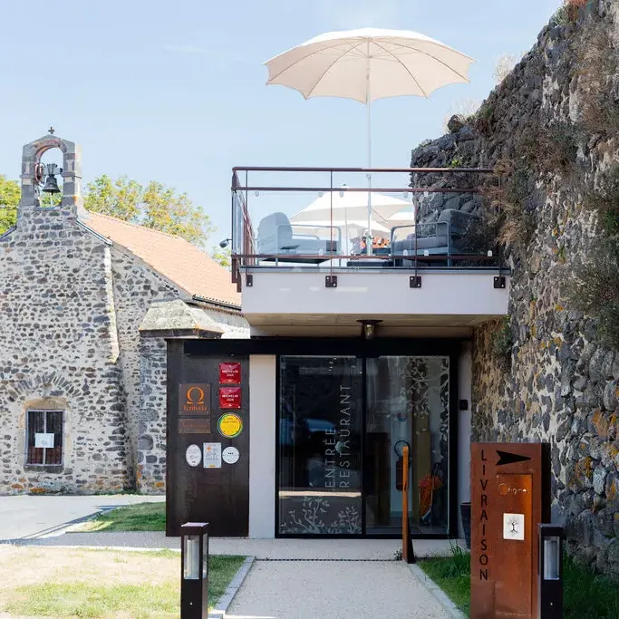 A modern restaurant with a rooftop terrace, adjacent to a small stone church, under a clear sky