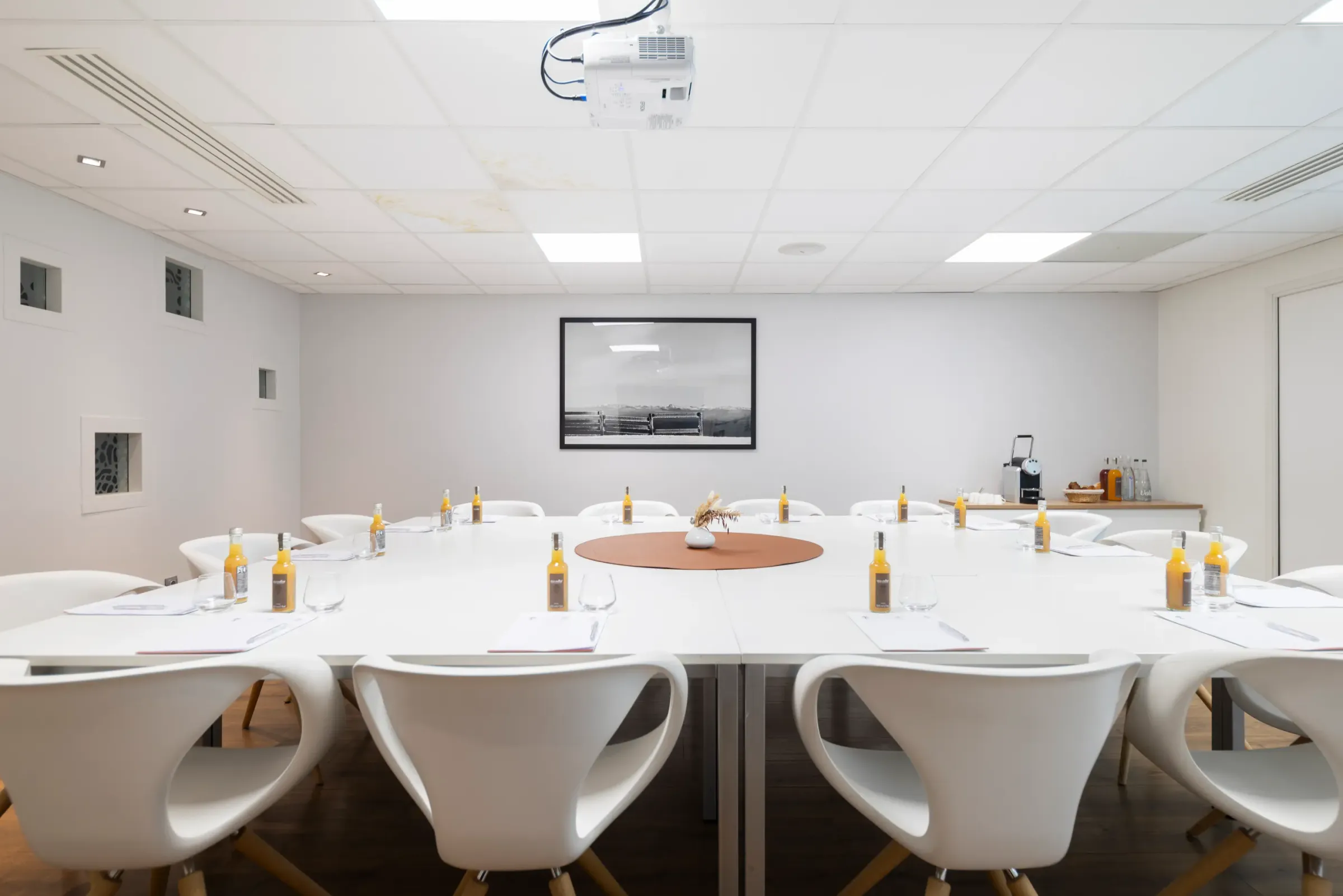 Salle de réunion avec une table ronde, des chaises blanches, des bouteilles d'eau et un projecteur au plafond