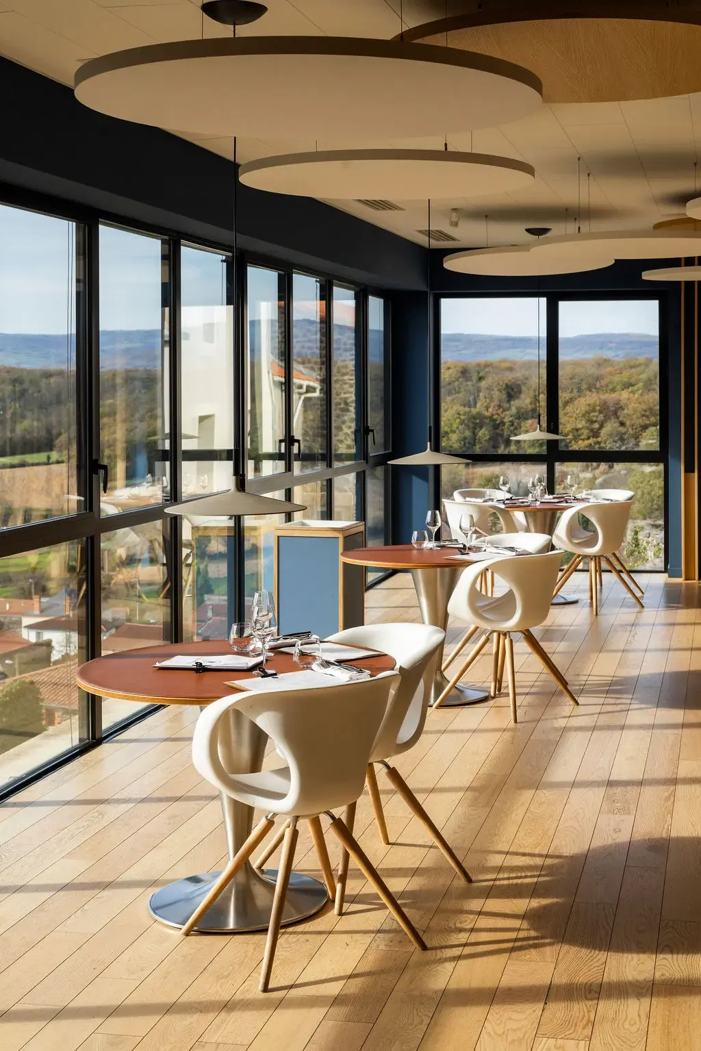Restaurant avec tables et chaises modernes disposées près de grandes baies vitrées offrant une vue panoramique sur un paysage extérieur