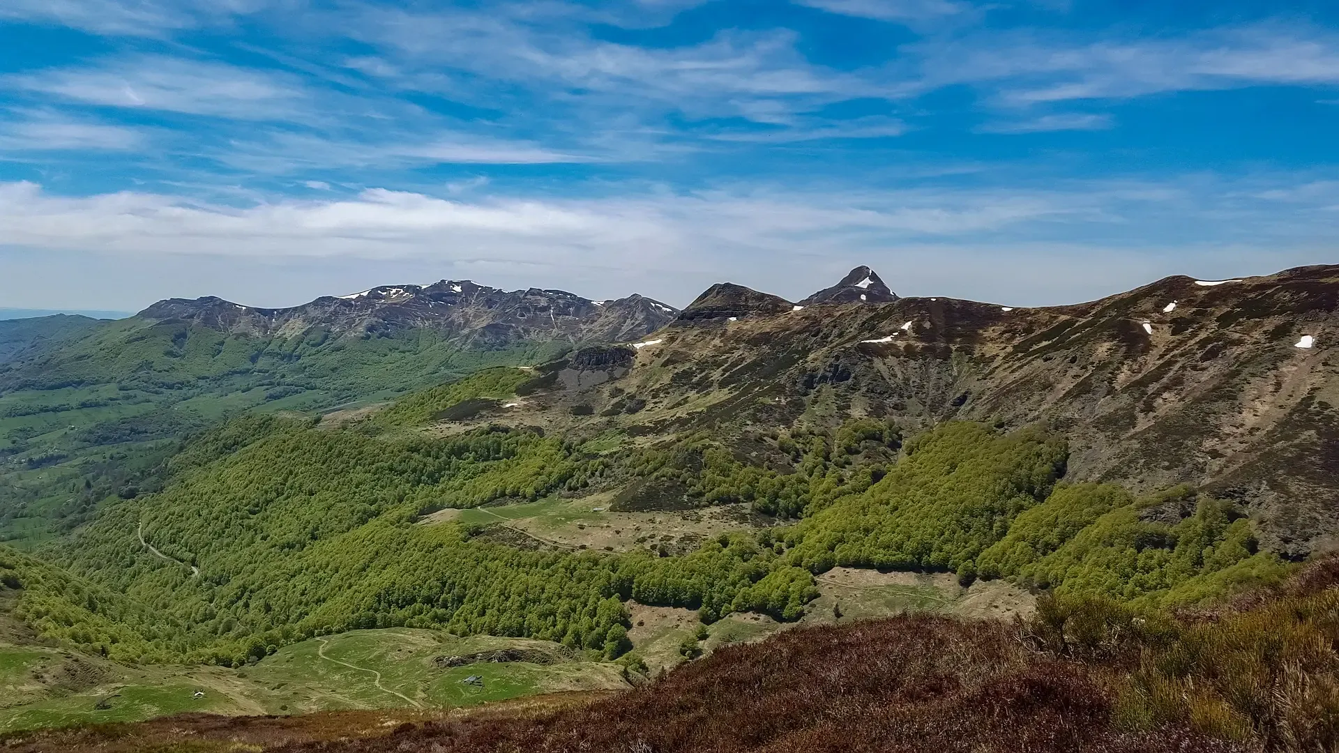 Panorama of lush green mountains with rocky peaks under a partly cloudy sky