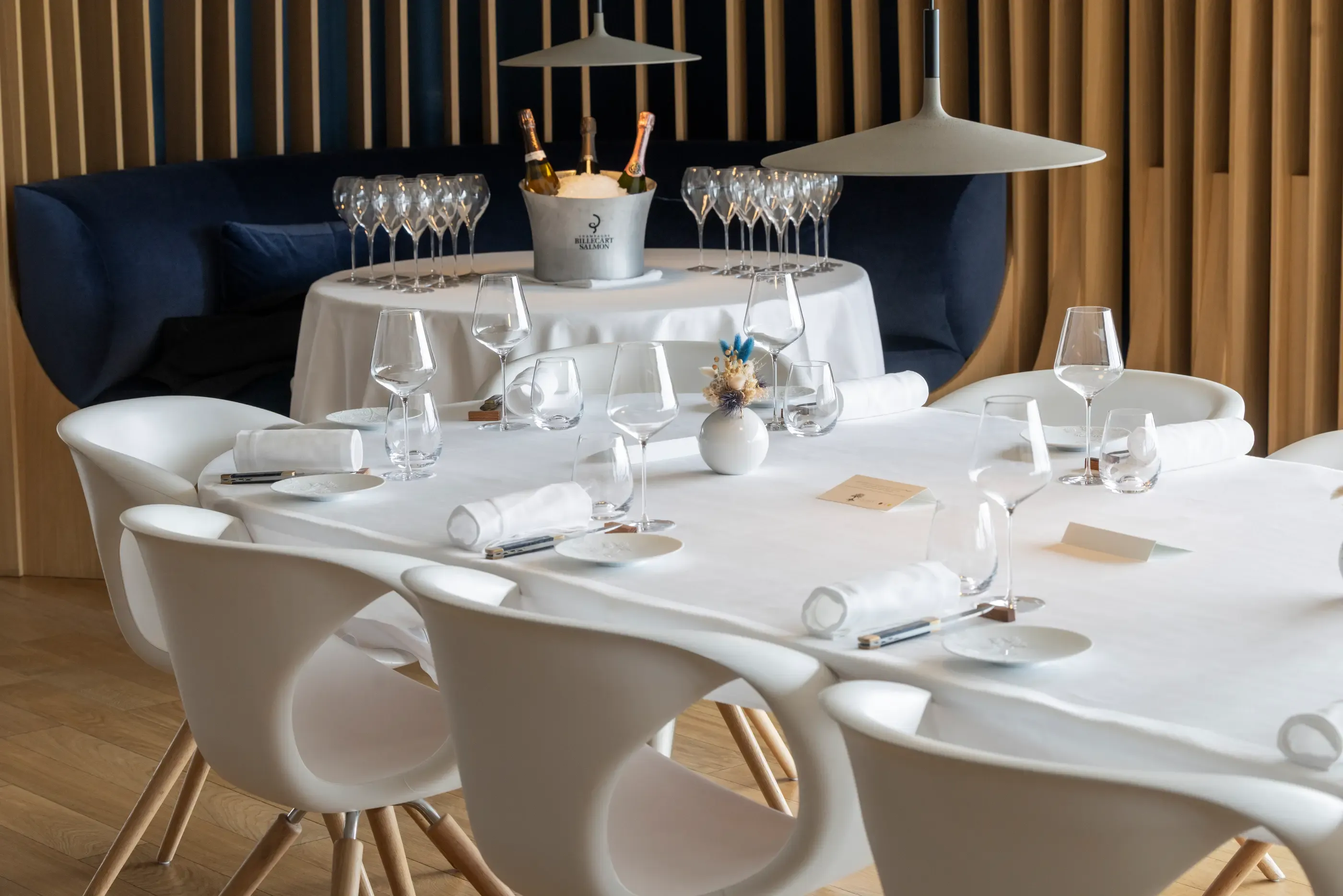 Tables rondes avec verres à vin, serviettes et bougies, dans un restaurant élégant avec des chandeliers et des canapés en arrière-plan