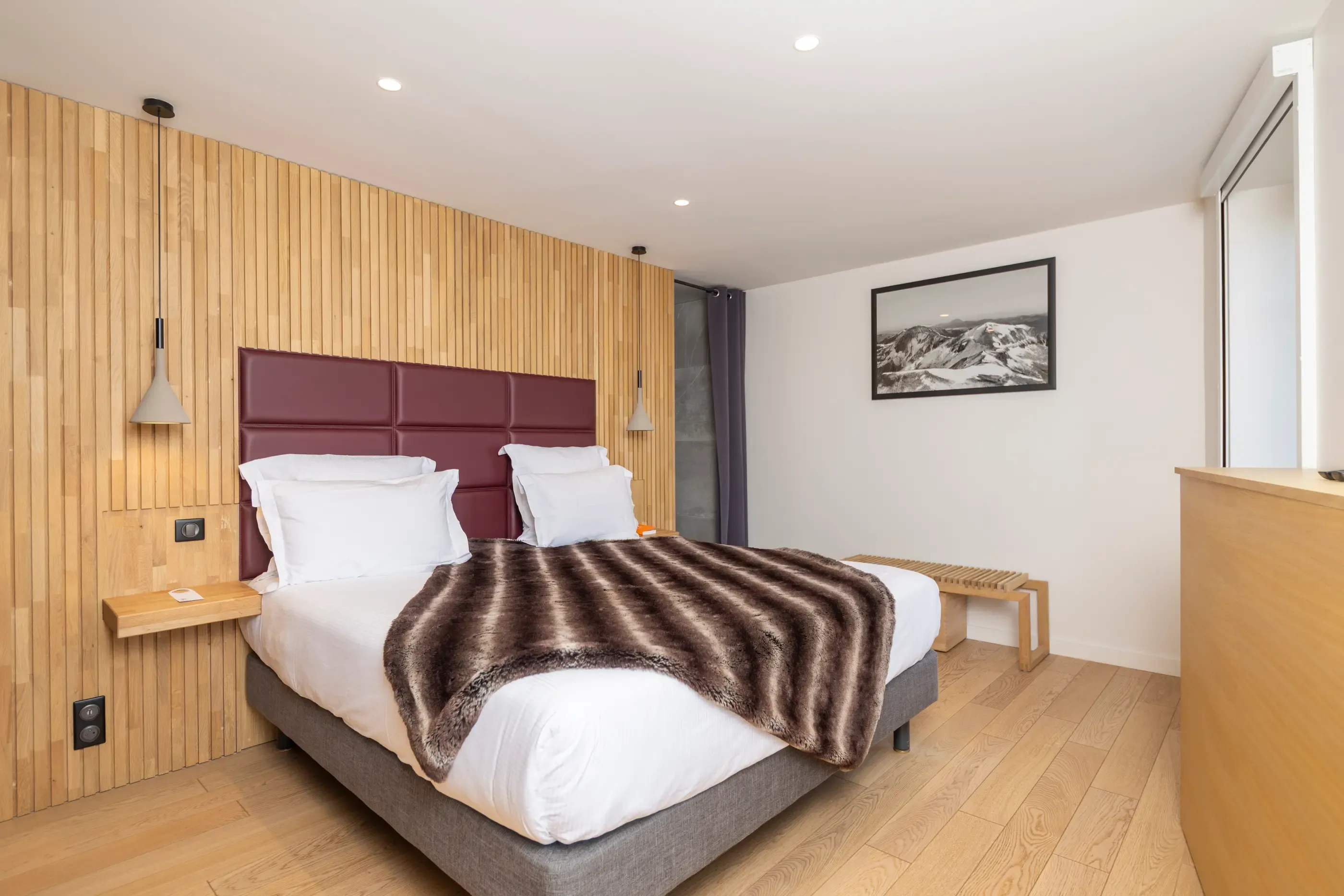 Bedroom with a double bed, a brown leather headboard, a patterned blanket, and light wooden walls.