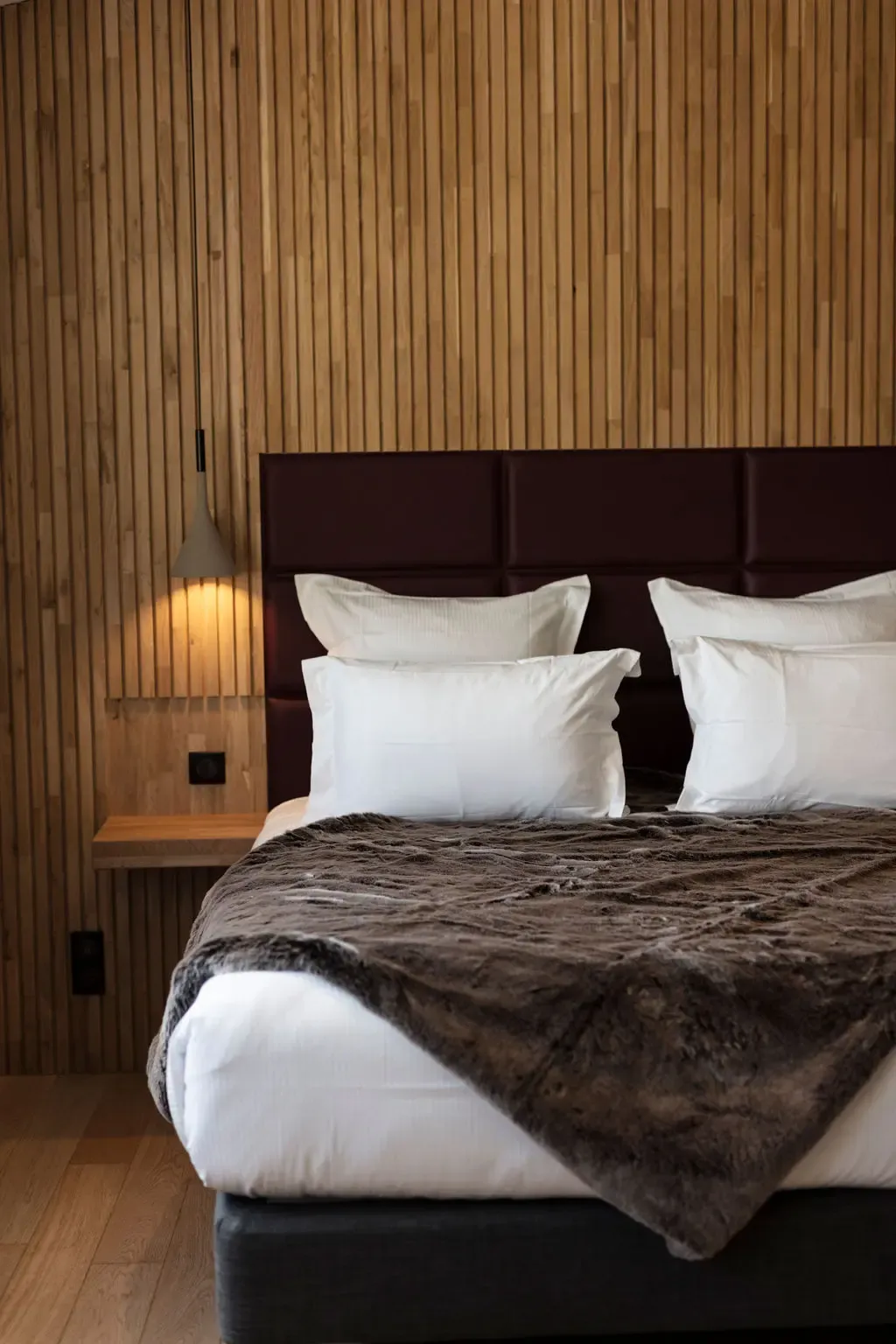 Bed with a brown leather headboard, white sheets, and a gray blanket in a room with wooden walls